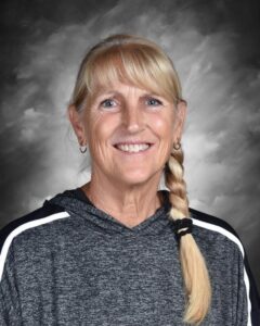 A smiling woman with long blonde hair in a braid, wearing a gray hoodie with white stripes, against a cloudy background.