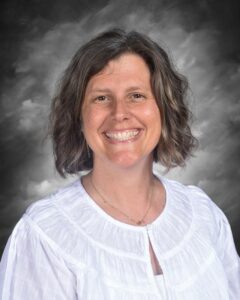 Mujer sonriente con cabello rizado y blusa blanca, sobre un fondo gris.