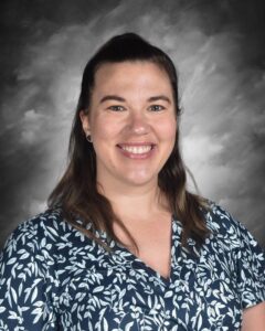 A smiling woman with long dark hair wearing a floral-patterned shirt, set against a gray background.