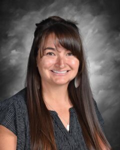 Smiling woman with long brown hair, wearing a striped shirt, against a gray background.