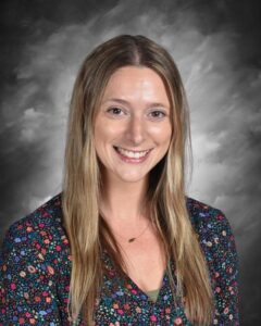 Smiling woman with long hair wearing a floral top, against a gray background.