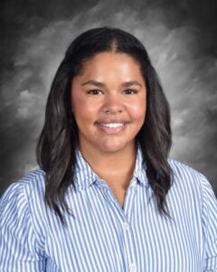 A smiling woman with dark hair in a striped shirt poses against a gray backdrop.