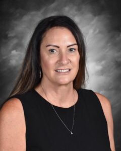 A woman with long dark hair wearing a black sleeveless top smiles, set against a gray background.