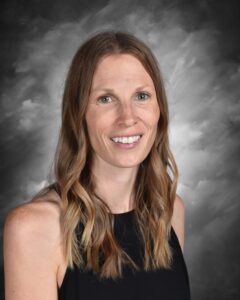 A smiling woman with long, wavy hair, wearing a black sleeveless top, against a gray background.