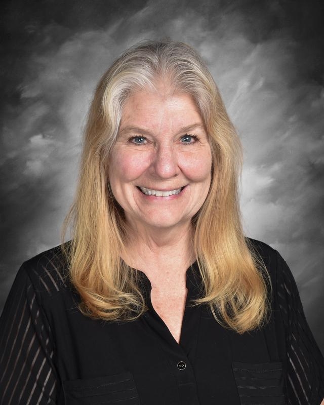 Smiling woman with long, light brown hair, wearing a black blouse, against a gray background.
