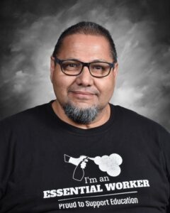 Portrait of a man with glasses and a beard, wearing a black shirt that reads "I'm an ESSENTIAL WORKER."