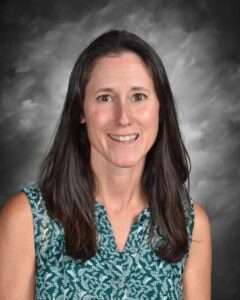 Smiling woman with long dark hair, wearing a green patterned blouse, against a gray background.